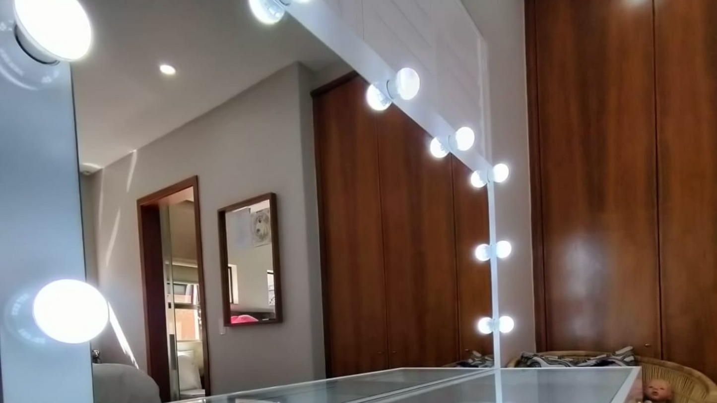 Mirror with light bulbs along the edge in a room with wooden cabinets and a framed picture on the wall.
