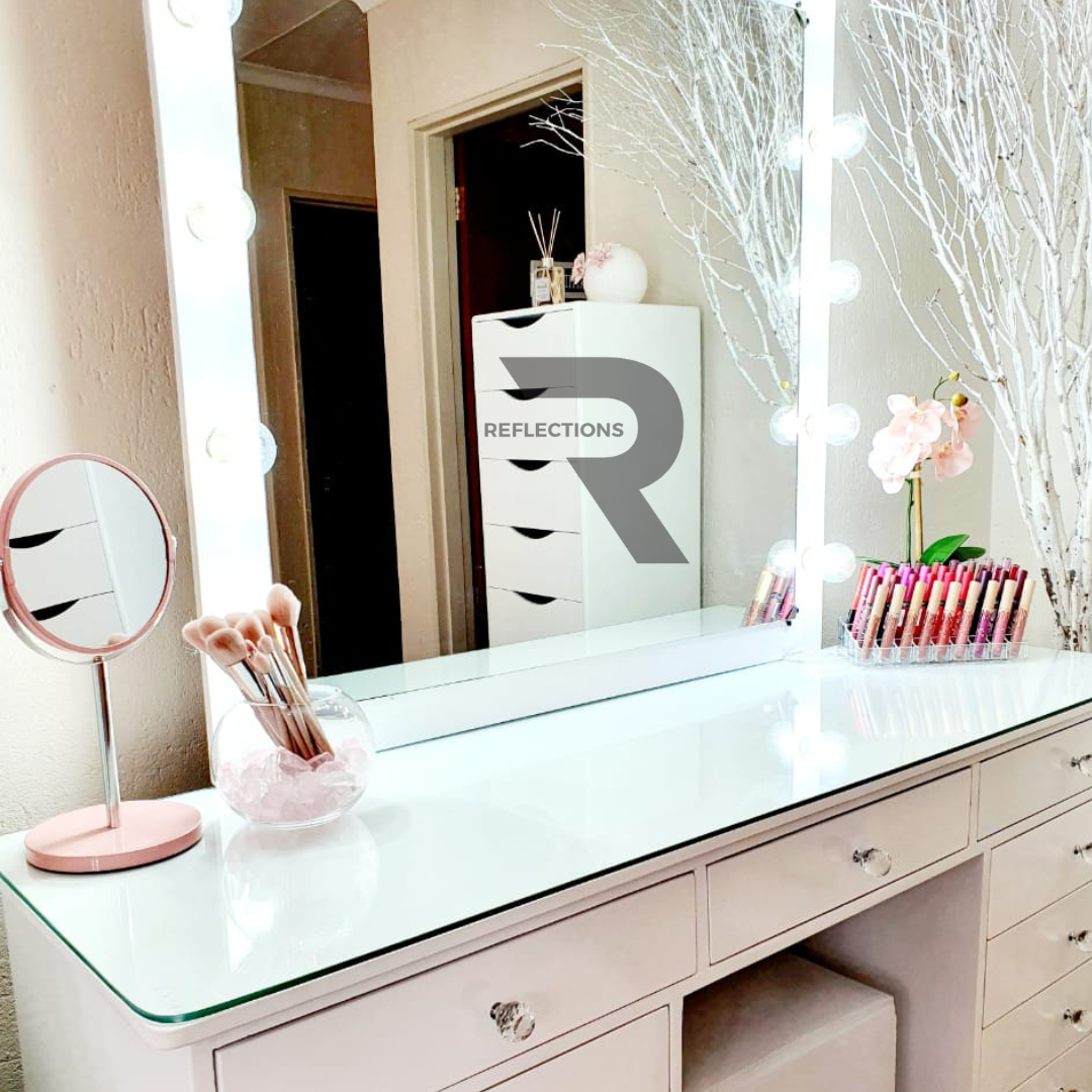 A white queen vanity set with a solid top and a large circular mirror, featuring crystal knobs and a pink flower vase with a reflection in the mirror.