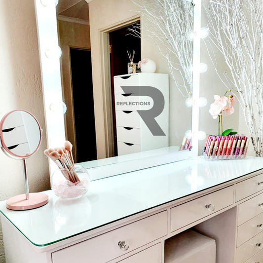 A white queen vanity set with a solid top and a large circular mirror, featuring crystal knobs and a pink flower vase with a reflection in the mirror.